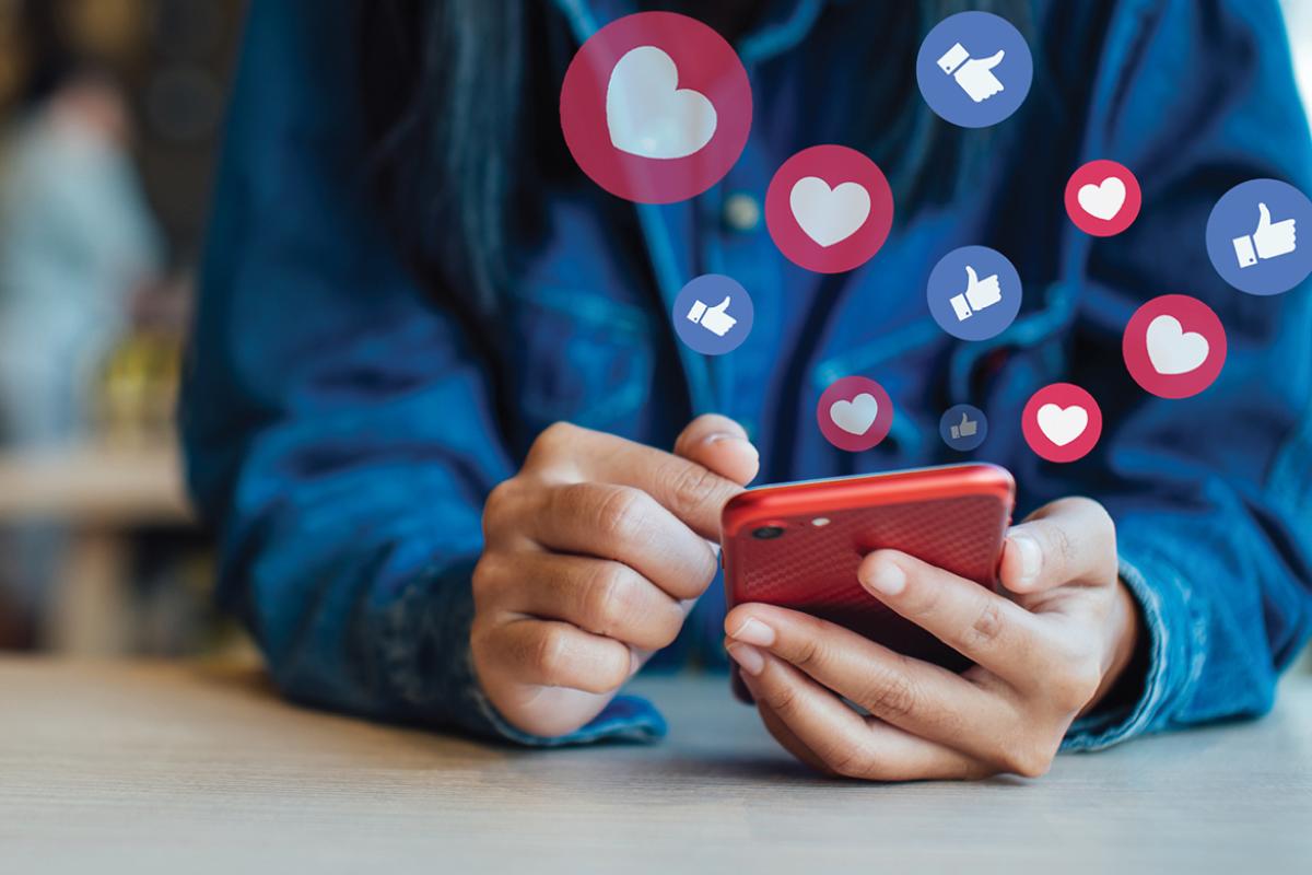 Photo illustration close-up of a person using a smart phone with a number of social media style likes and loves hovering over the phone.