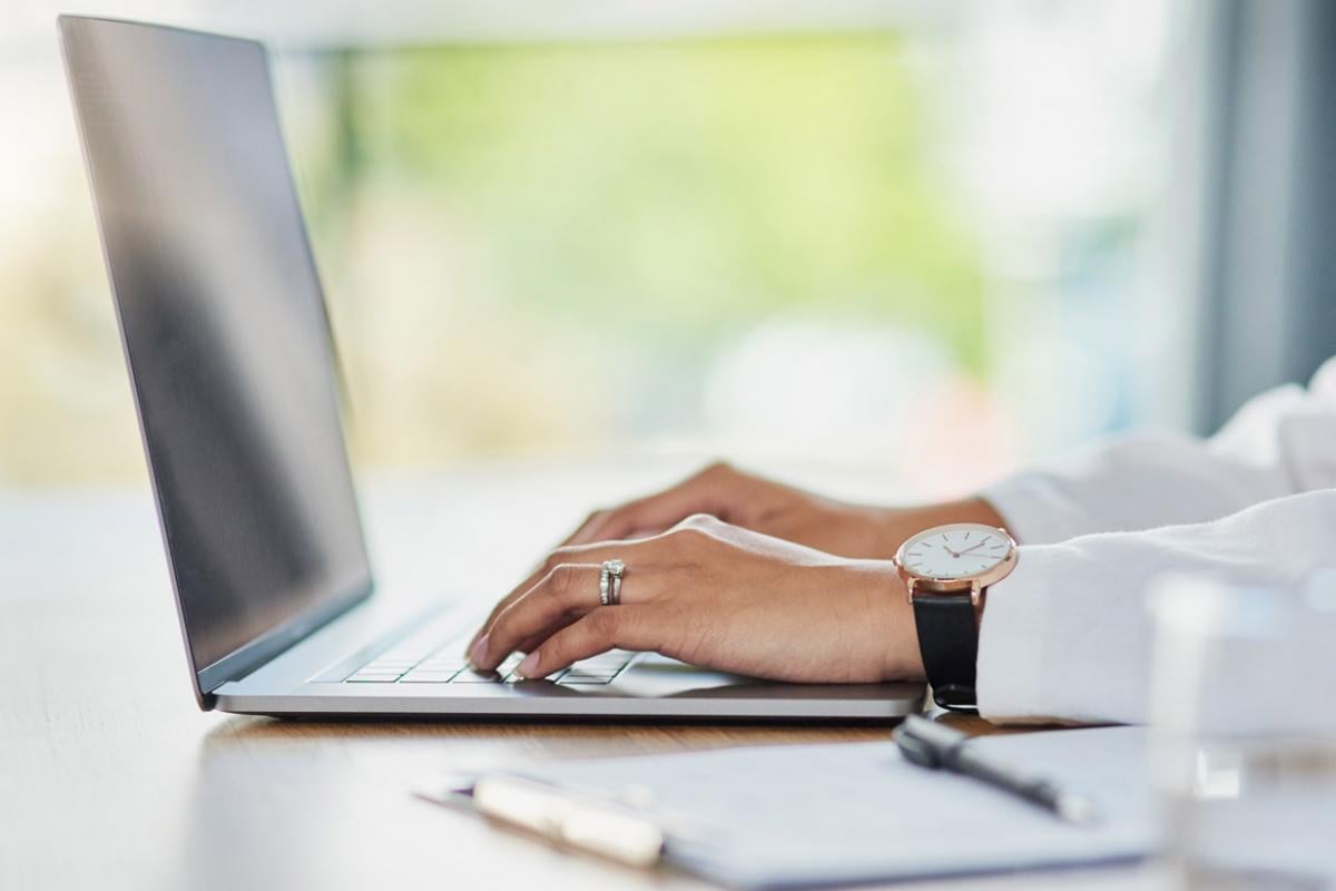 Close-up of a health care worker's hands working at a laptop.
