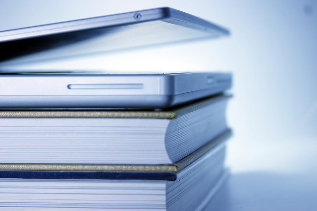 Slightly open laptop lying on top of stack of books