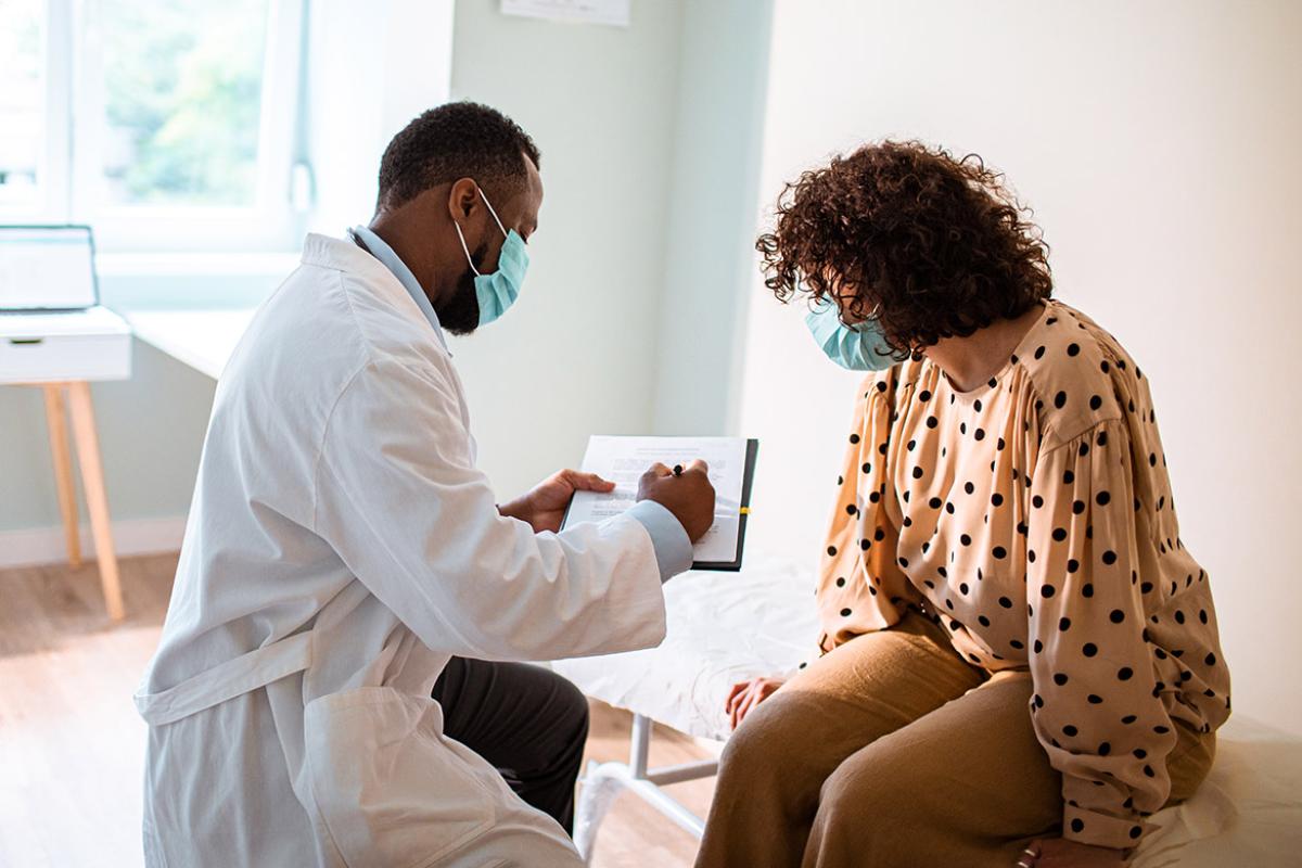 Physician going over examination notes with patient, both wearing masks.