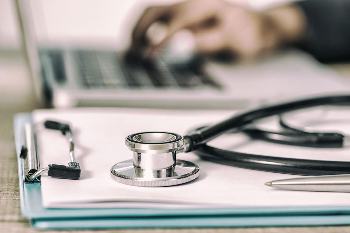 Stethoscope with clipboard and laptop on desk