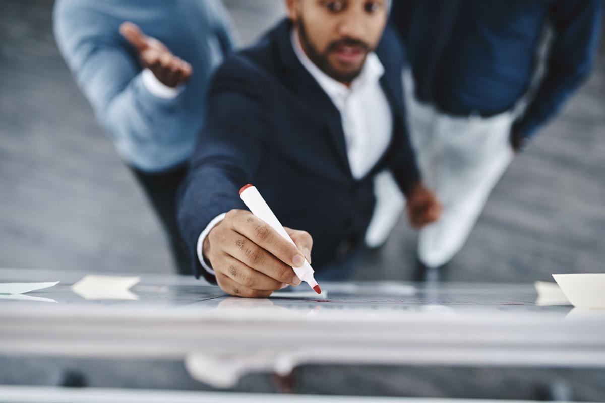 Three businesspeople brainstorming together on a whiteboard in an office