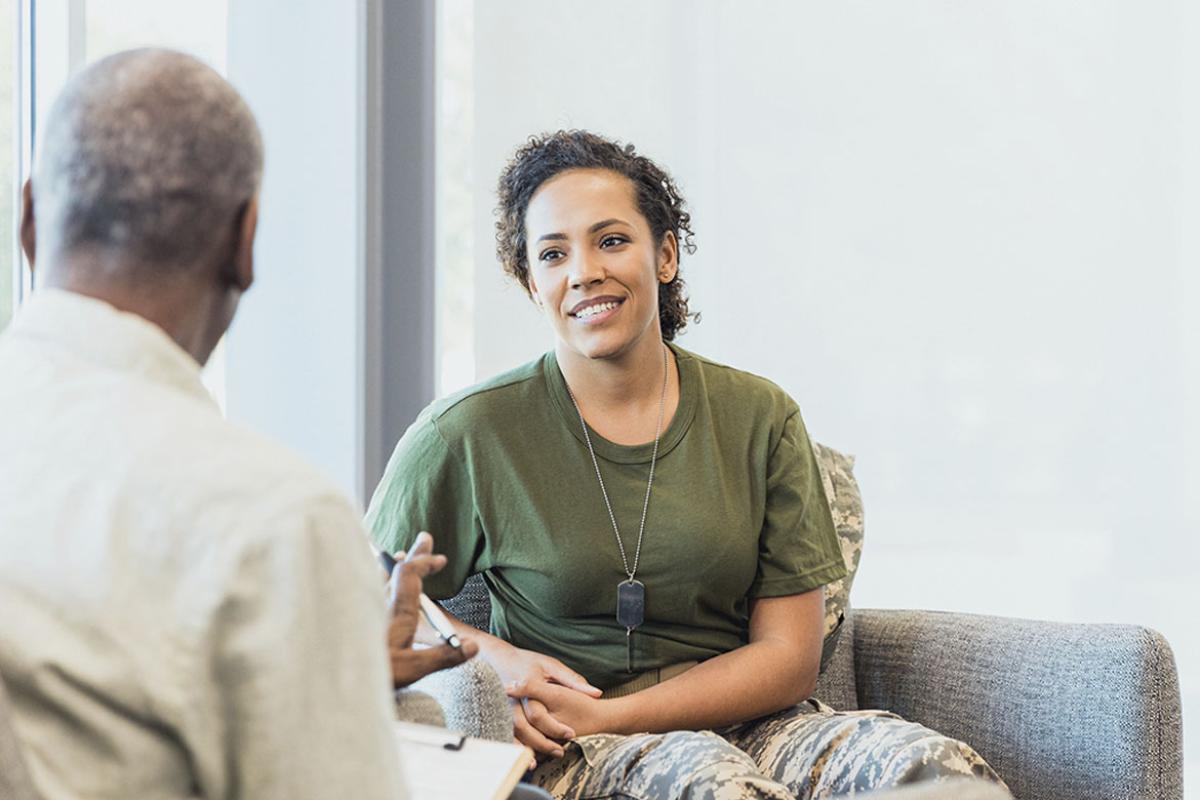 Soldier smiles as another person gestures and speaks