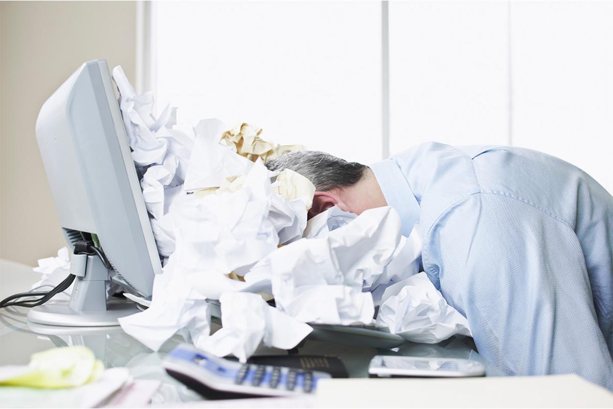 Person with their head on a desk, surrounded by crumpled paper
