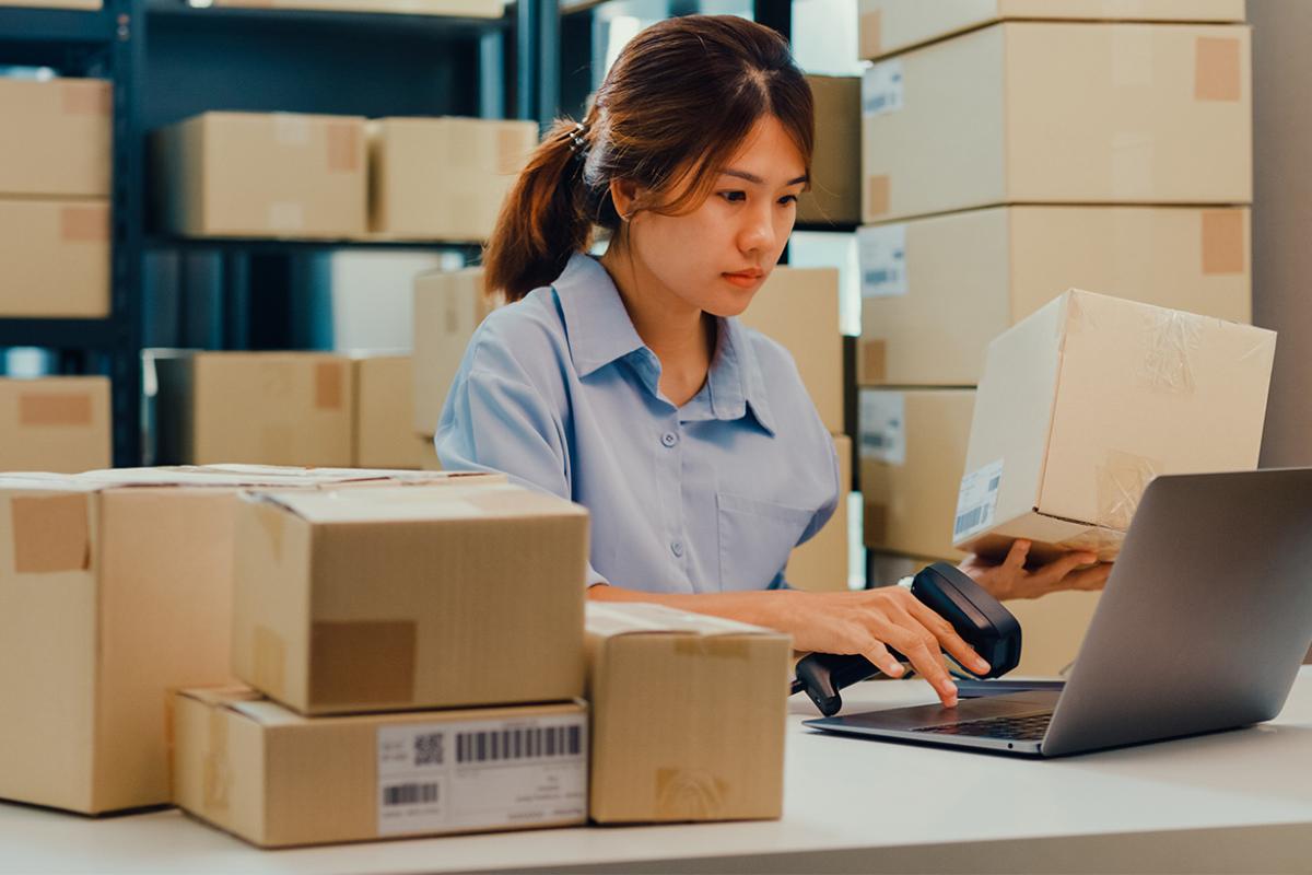 Businesswoman sits front of shelf using barcode to scan order detail