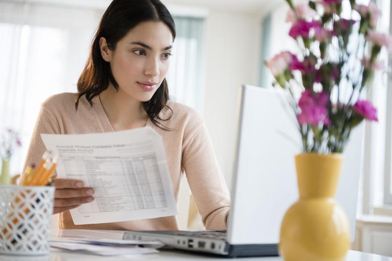 Person holding a document and working in front of a laptop