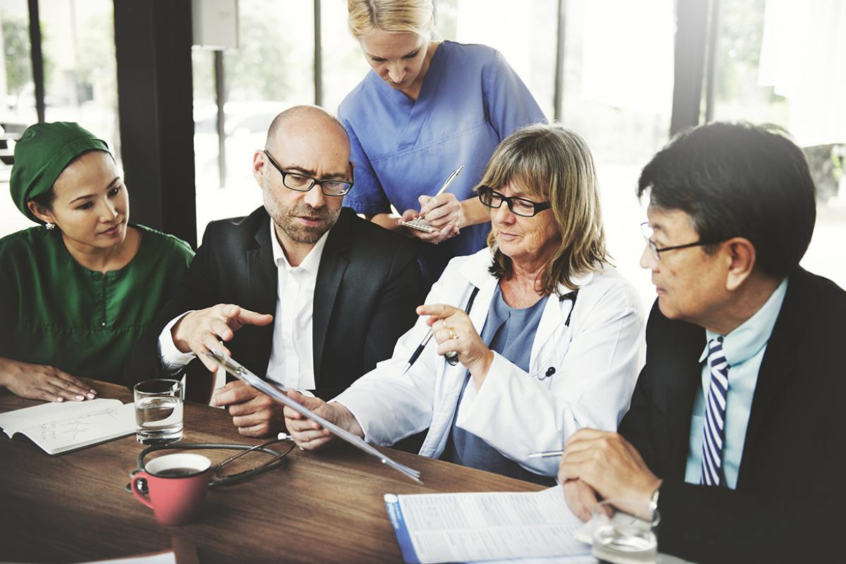 A physician sits at a table and reviews paperwork with her staff and the leadership team of her medical practice.