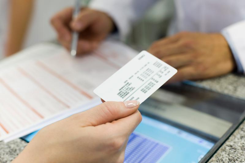 Woman handing an insurance card to a doctor who is reviewing paperwork