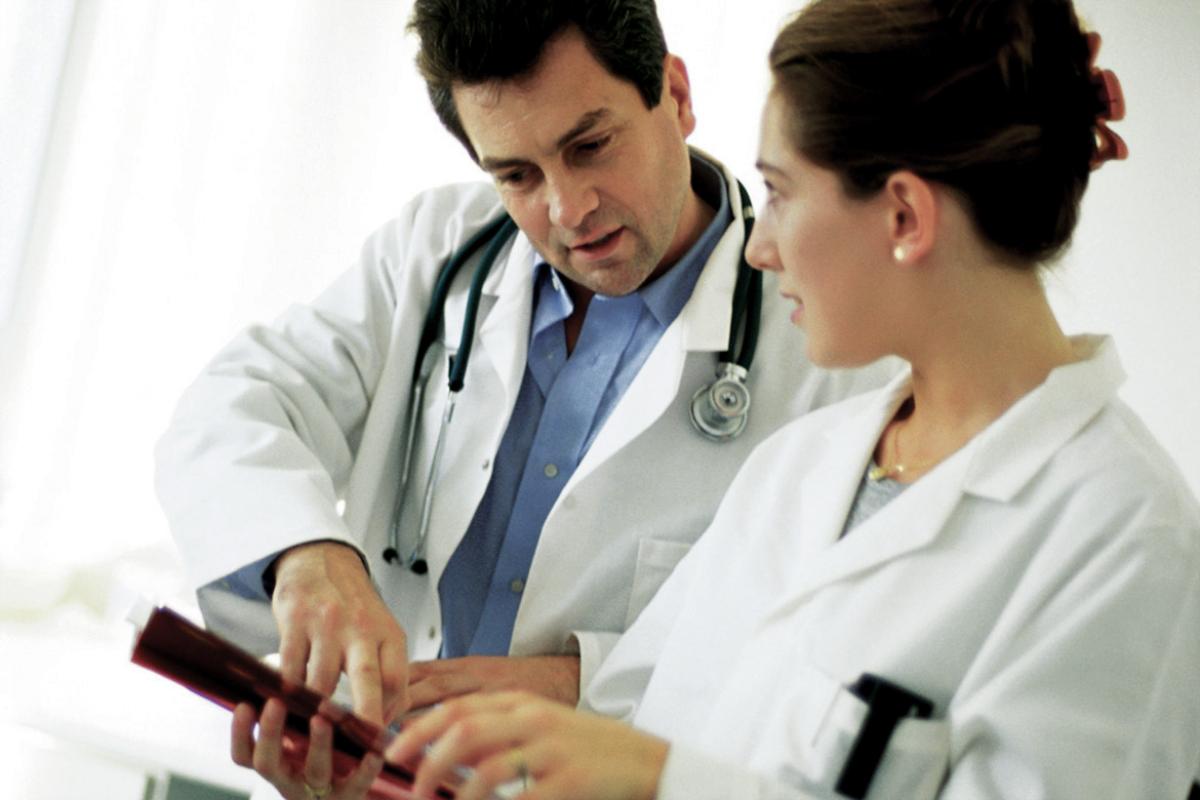 A man and a female physician look at the screen of a tablet.