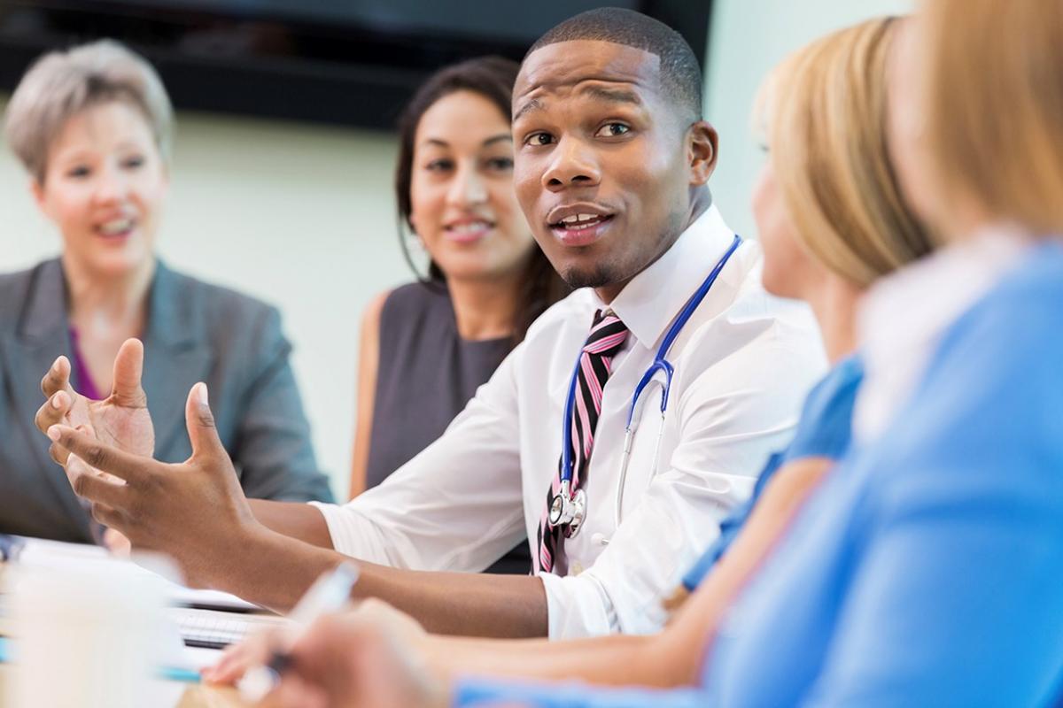 Physician sitting at a table talking to health care professionals participating in health care system.