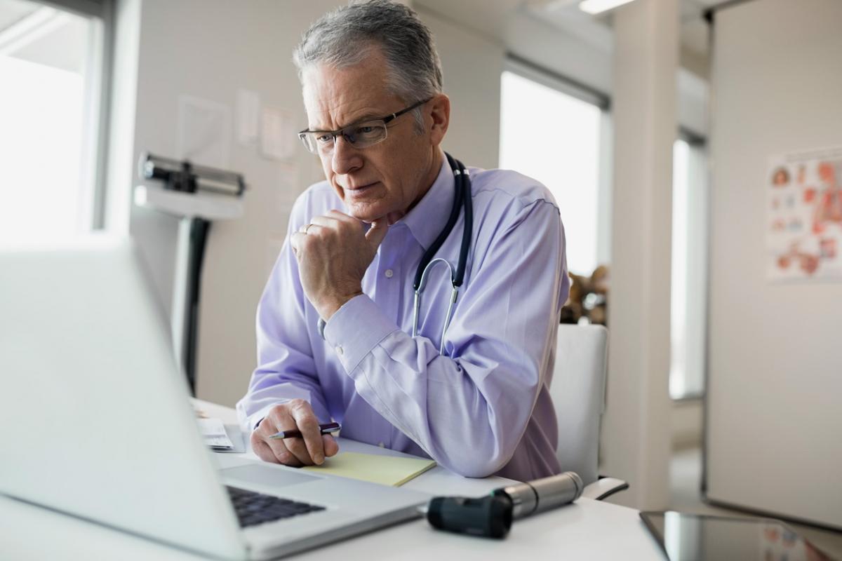 An older physician fill out charts on his laptop.