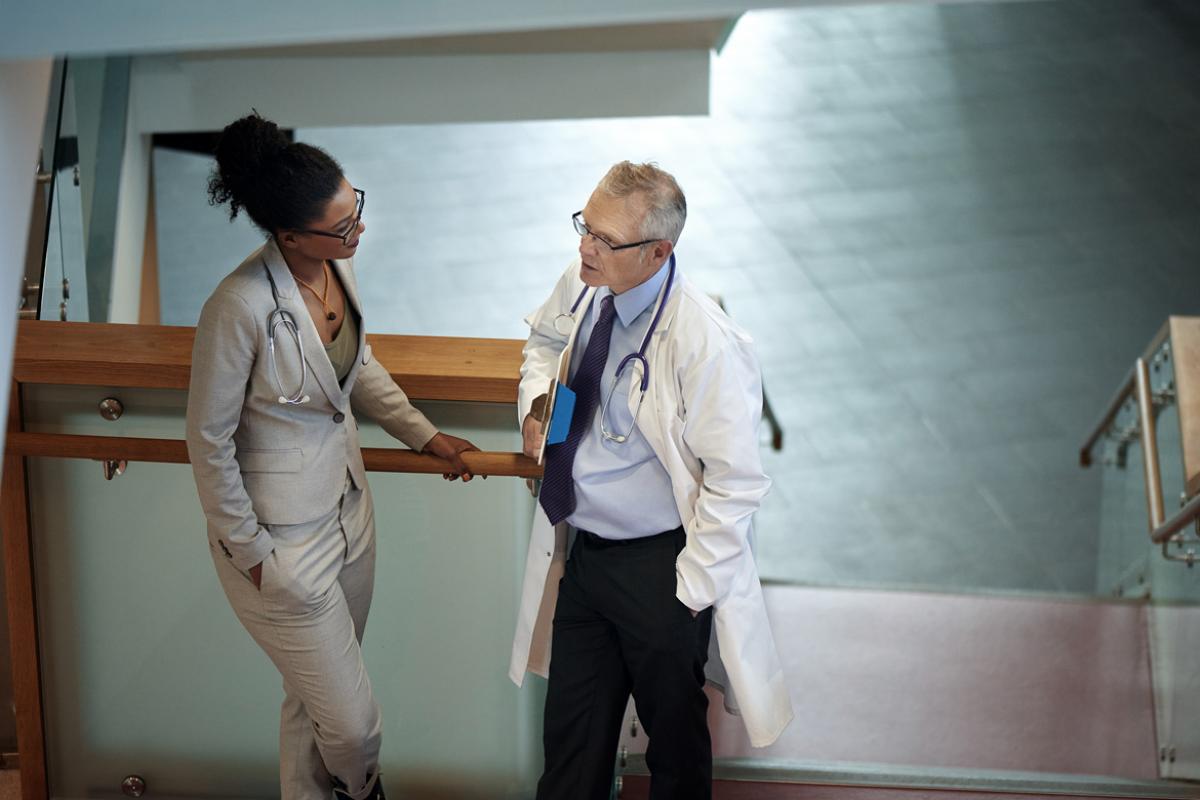 A younger female and older male physician speak about medicare payment reform in a quiet area of a hospital.