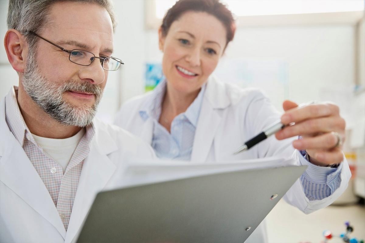 Two physicians reviewing notes on a clipboard.