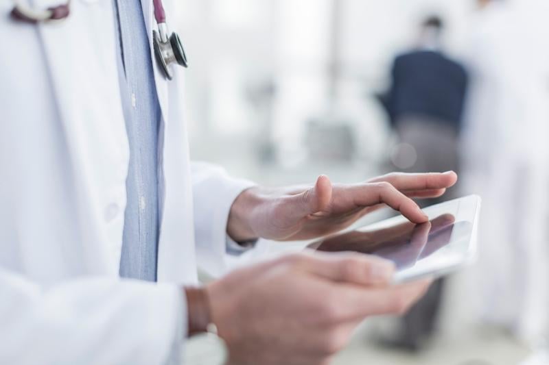 A male doctor putting his finger on a tablet screen
